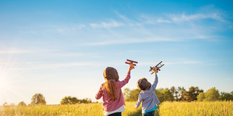 Boy and girl playing with wooden planes on the field in sunset.
