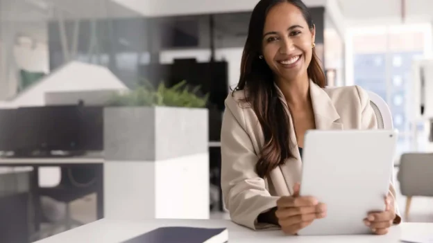 A woman, professionally dressed, smiles in an office environment.