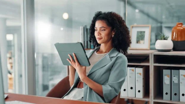 A business professional sits at her desk, working on her tablet.