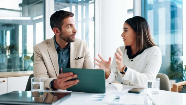 Two office workers discussing something in front of a tablet.