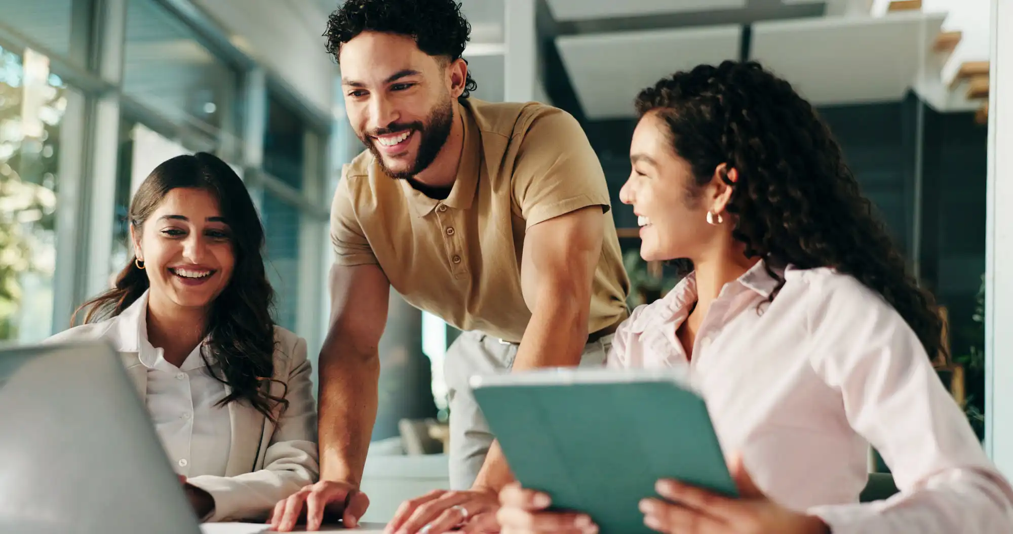 Three smiling office employees gathered around a laptop, at a desk.
