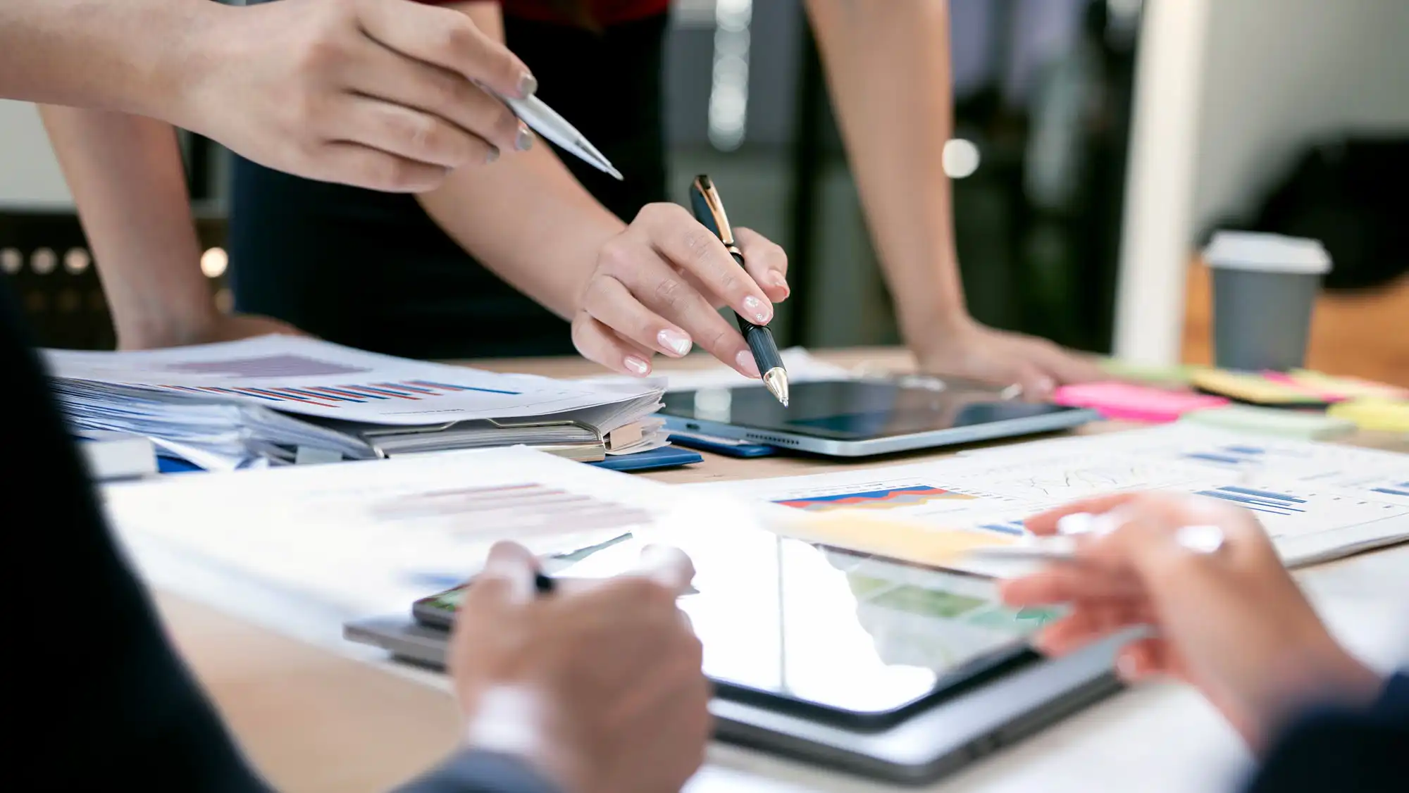 A closeup view of a conference room table, with papers and documents being observed by various employees.