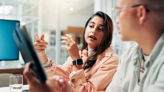 A woman and a man observe information on a tablet. The woman is explaining something to the man.