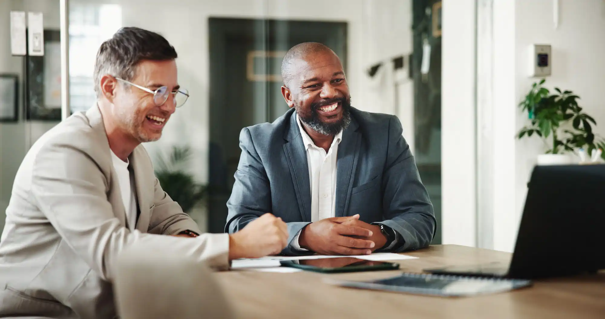 Two businessman observing something on a laptop computer. Both men are smiling.