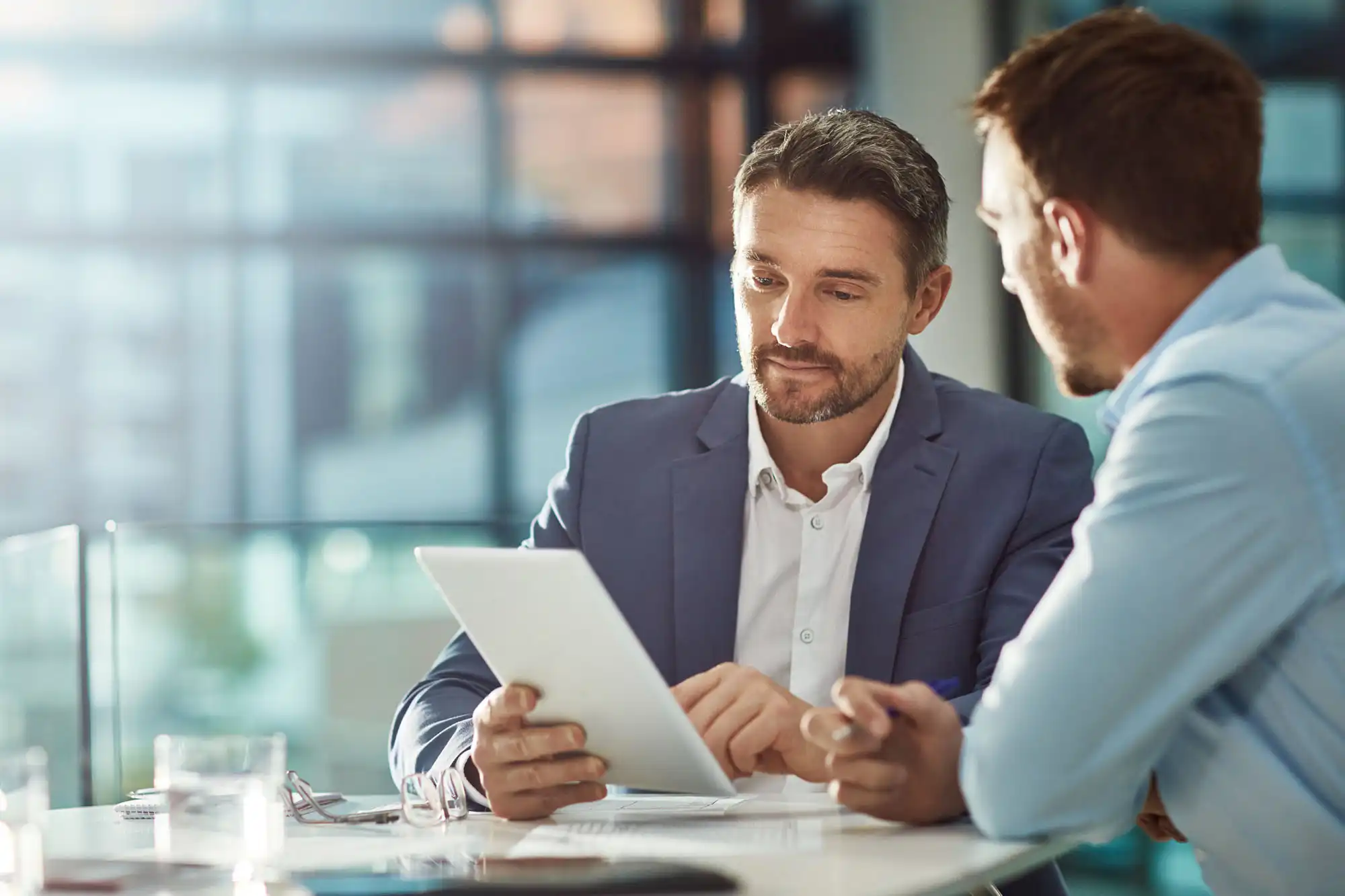 Two businessmen typing some information in on a tablet. Both men are focused.