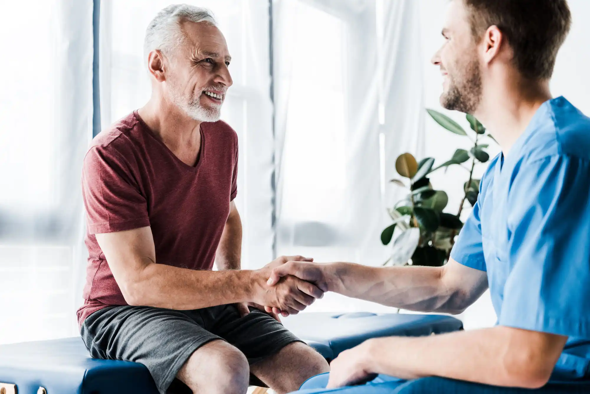 A smiling older man shakes hand with a young healthcare professional.