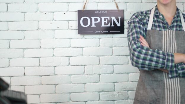 A cafe business owner stands next to an open sign