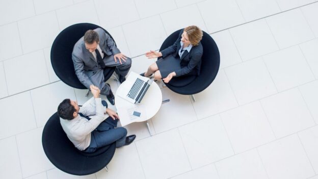 Three employees sitting together collaborating on computers