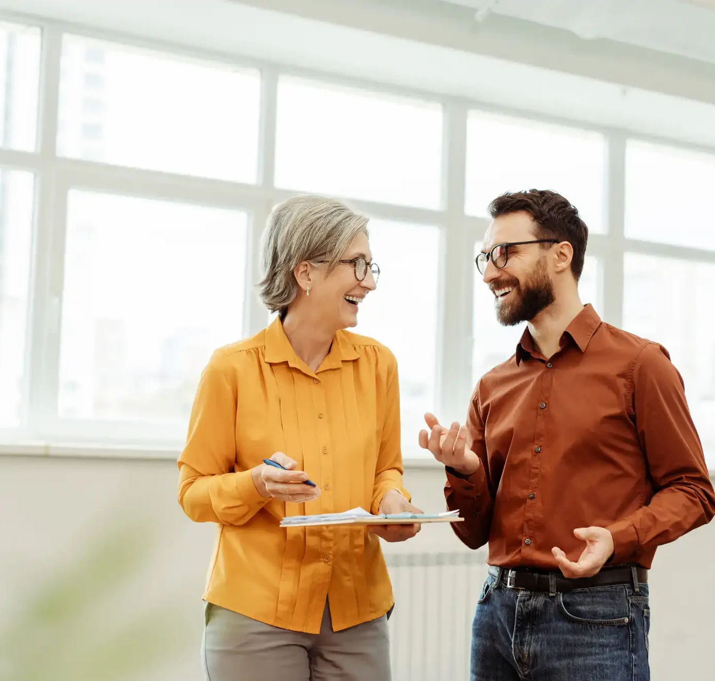 Two smiling business professionals in an office settings, laughing.