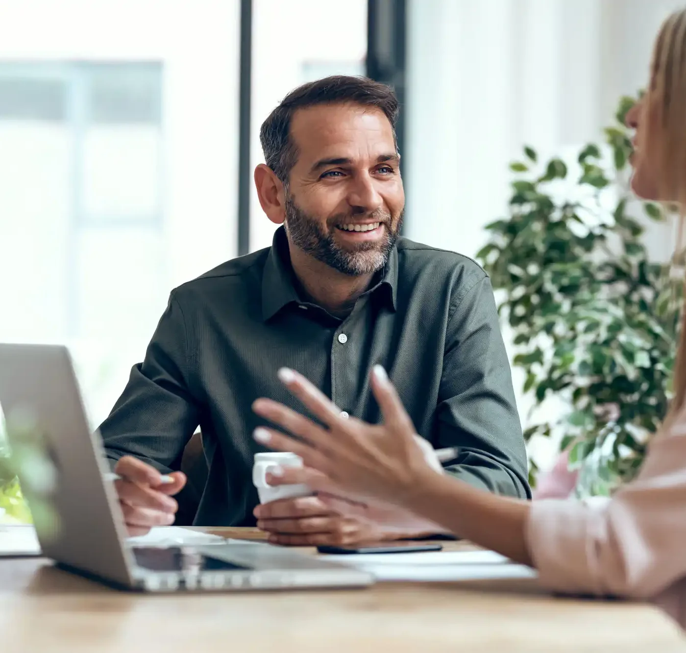 A man smiles while conversing with his co-worker in an office environment.