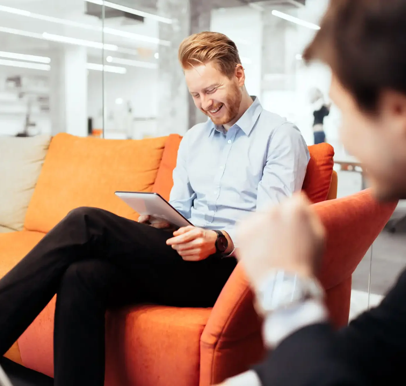 A man smiles while sitting on a couch, reviewing some information on a tablet.