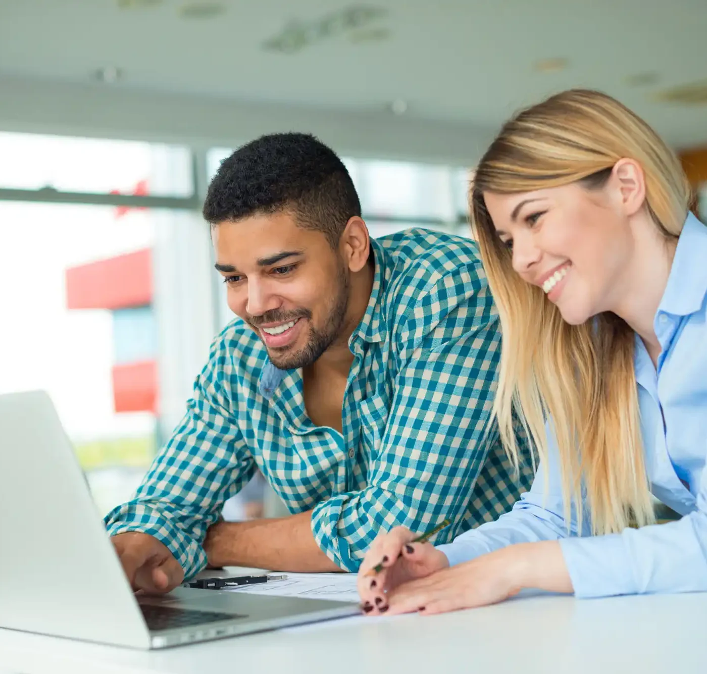 Two office workers smiling while observing some information on a laptop computer.